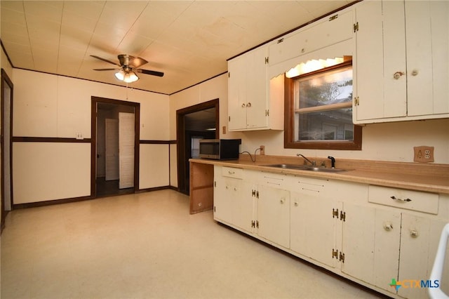 kitchen featuring a sink, stainless steel microwave, white cabinetry, light countertops, and light floors