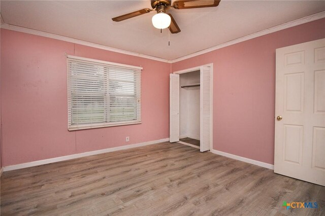 unfurnished bedroom featuring a closet, wood finished floors, baseboards, and ornamental molding