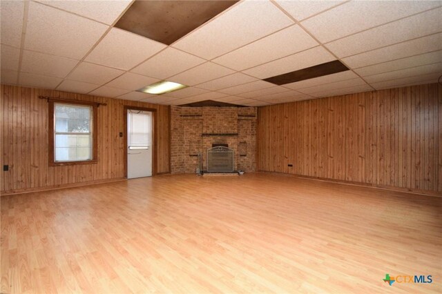 unfurnished living room featuring a paneled ceiling, wood walls, and light wood finished floors