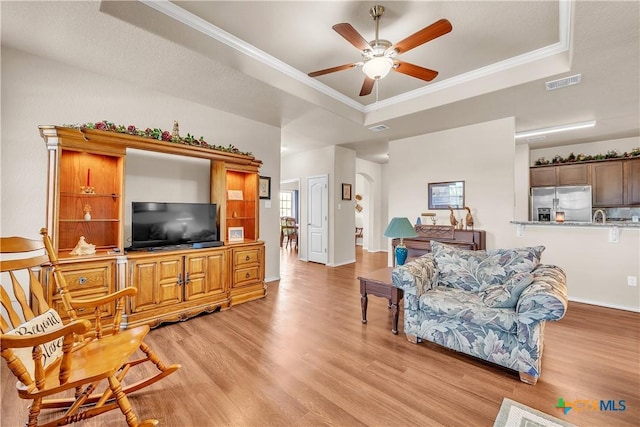 living room featuring crown molding, light wood-type flooring, ceiling fan, and a raised ceiling