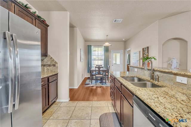 kitchen with light stone countertops, sink, pendant lighting, and stainless steel appliances