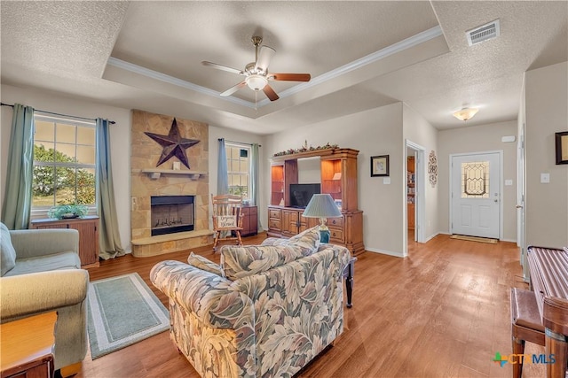 living room with light hardwood / wood-style flooring, ornamental molding, a fireplace, and a tray ceiling