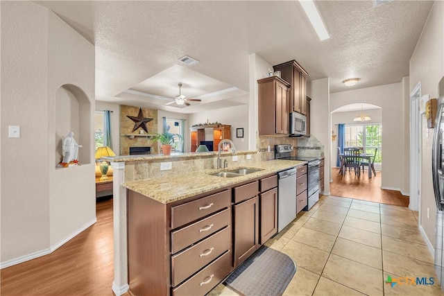 kitchen with kitchen peninsula, sink, light tile patterned floors, light stone counters, and stainless steel appliances