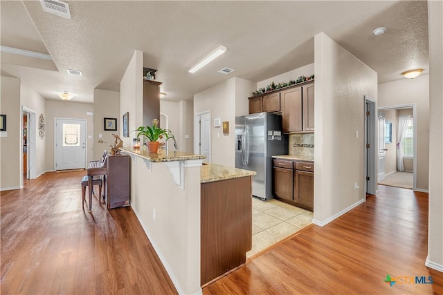 kitchen featuring light stone countertops, a textured ceiling, a kitchen breakfast bar, stainless steel fridge with ice dispenser, and light hardwood / wood-style flooring