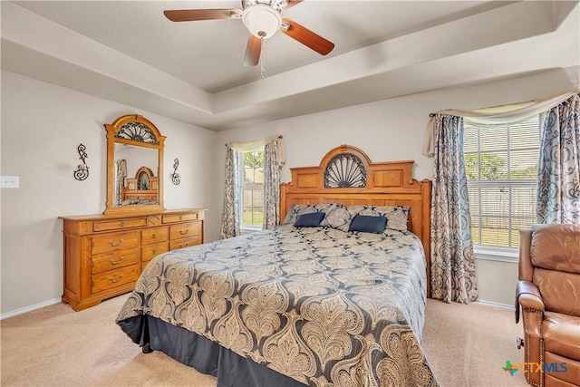 bedroom with ceiling fan, light colored carpet, and a tray ceiling