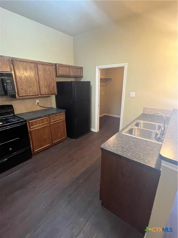 kitchen with brown cabinets, black appliances, a sink, dark countertops, and dark wood-style floors