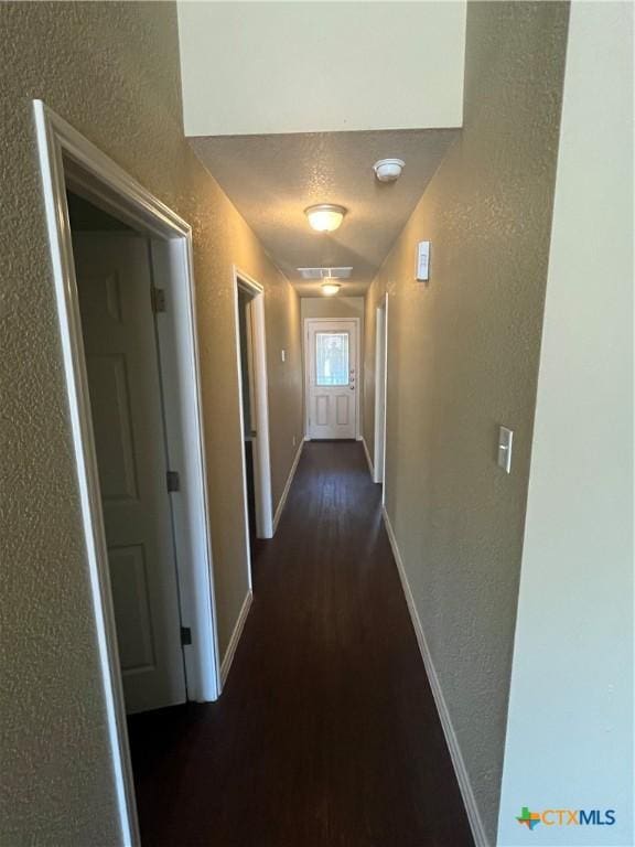 hall with a textured ceiling, baseboards, dark wood-type flooring, and a textured wall