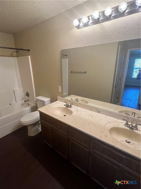 bathroom with a textured ceiling, double vanity, toilet, and a sink