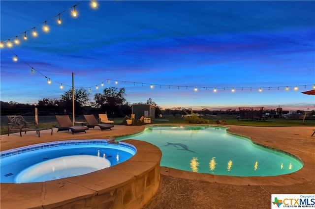 pool at dusk with a patio and an in ground hot tub