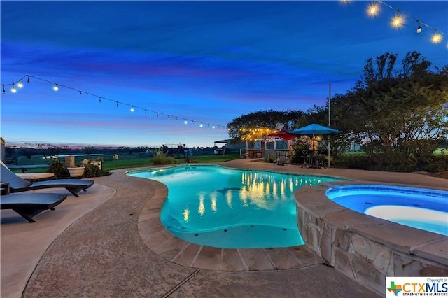 pool at dusk featuring a patio and an in ground hot tub