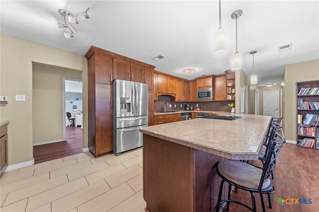 kitchen with appliances with stainless steel finishes, hanging light fixtures, a kitchen breakfast bar, sink, and backsplash