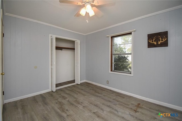 unfurnished bedroom featuring ceiling fan, crown molding, wood finished floors, baseboards, and a closet