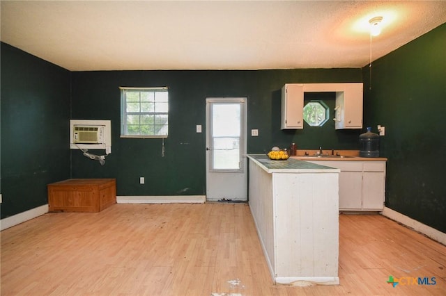 kitchen with a sink, white cabinets, light wood finished floors, and a wall mounted air conditioner