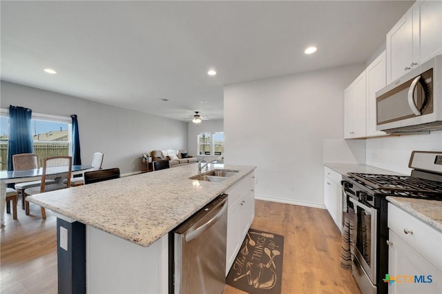 390 Lost Maples, New Braunfels, TX 78130 - kitchen with appliances with stainless steel finishes, a center island with sink, ceiling fan, light wood-style floors, and light stone counters