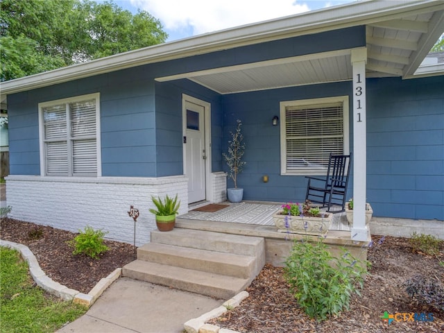 doorway to property with a porch and brick siding