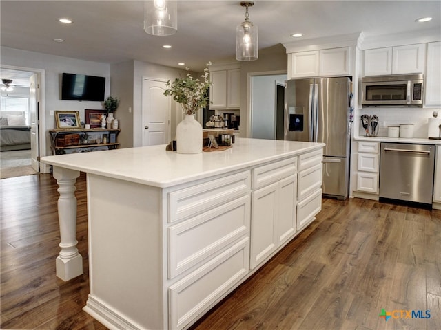 kitchen with a center island, decorative light fixtures, white cabinets, appliances with stainless steel finishes, and dark wood-style floors