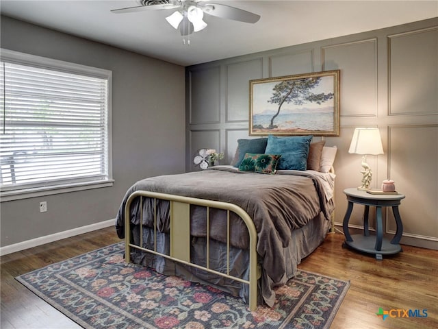 bedroom with wood finished floors, a decorative wall, a ceiling fan, and baseboards