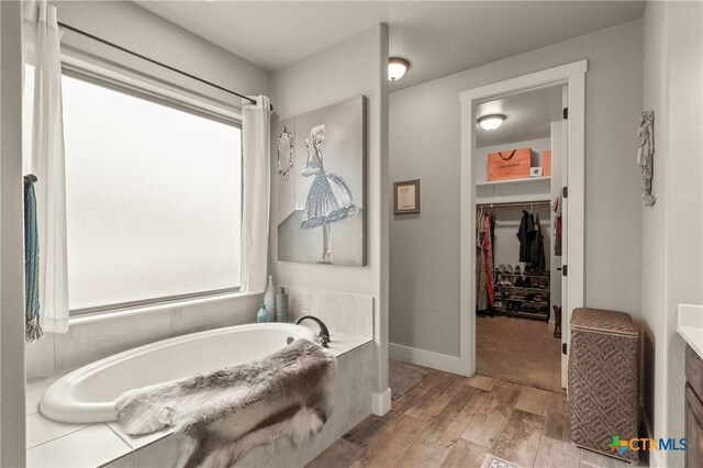 full bath with wood finished floors, a bath, and a spacious closet