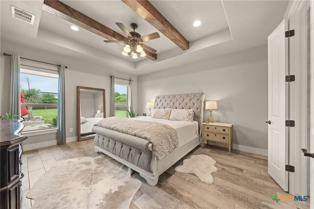 bedroom with visible vents, beam ceiling, a raised ceiling, baseboards, and light wood-style floors