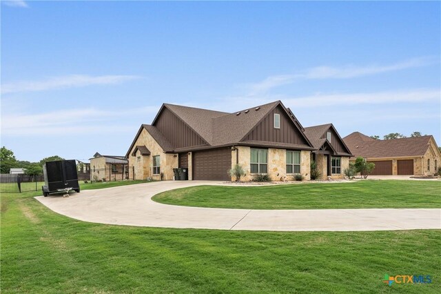 view of front of property featuring a front lawn, fence, stone siding, board and batten siding, and driveway