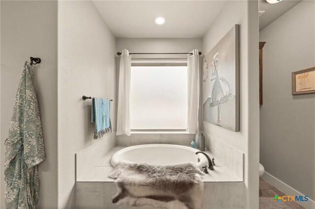 full bathroom featuring a garden tub, baseboards, and toilet