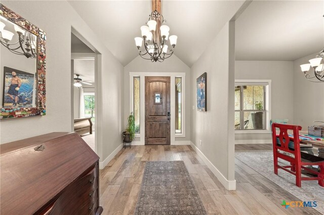 foyer entrance with baseboards, a chandelier, light wood-style flooring, and vaulted ceiling