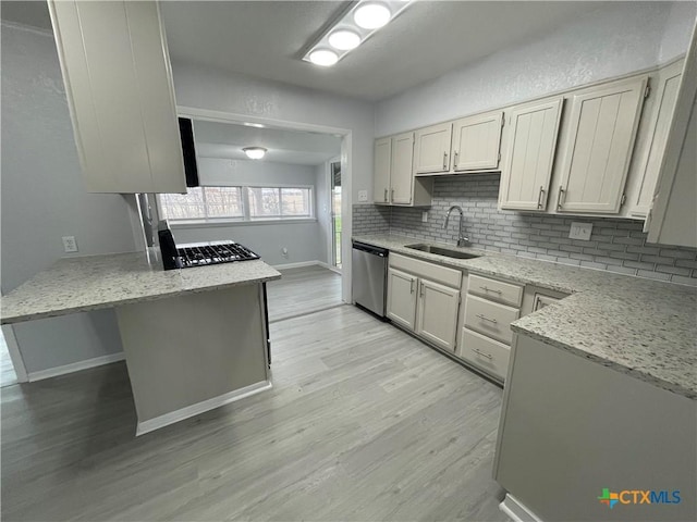 kitchen with light wood-style flooring, backsplash, a peninsula, stainless steel dishwasher, and a sink