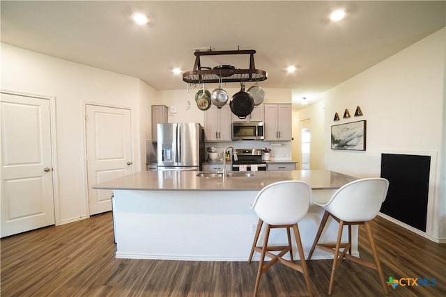 kitchen featuring a center island with sink, a sink, dark wood-style floors, appliances with stainless steel finishes, and light countertops