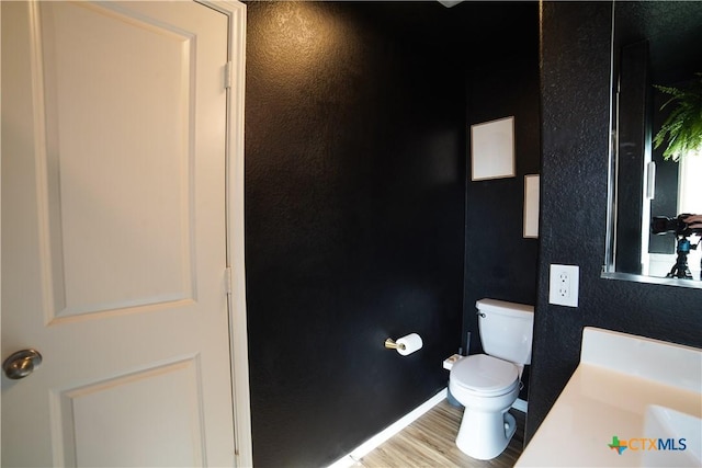 bathroom with toilet, wood finished floors, baseboards, and a textured wall