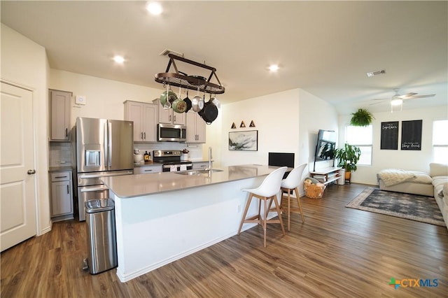 kitchen with a sink, backsplash, open floor plan, stainless steel appliances, and dark wood-style flooring