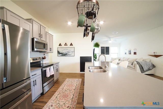 kitchen with backsplash, ceiling fan, appliances with stainless steel finishes, dark wood-style floors, and a sink