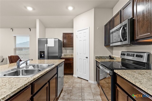 kitchen with light stone countertops, appliances with stainless steel finishes, sink, and dark brown cabinetry