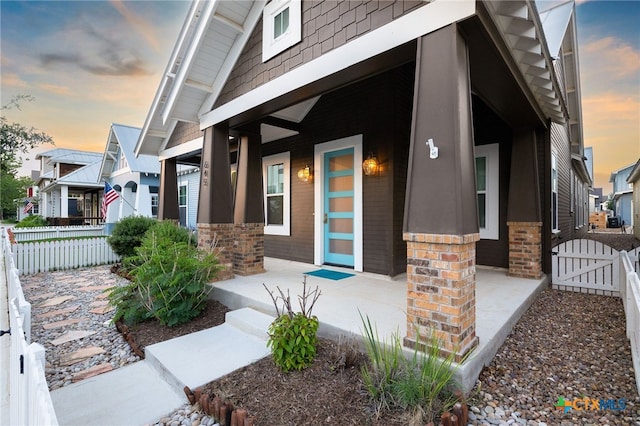645 Center Grn, New Braunfels, TX 78130 - exterior entry at dusk with a porch, brick siding, fence, and a gate