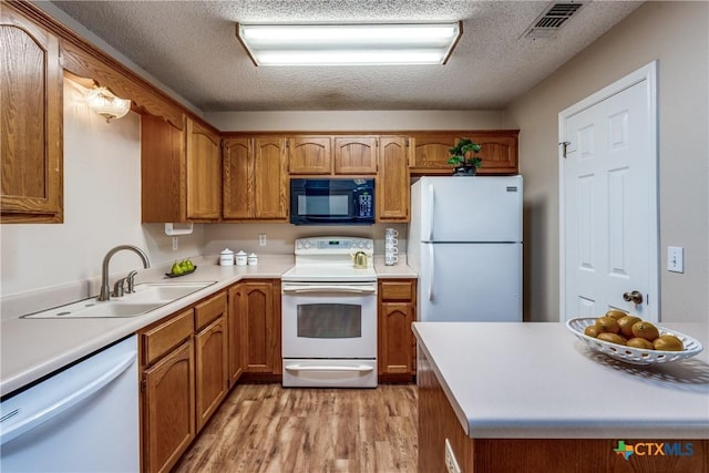 kitchen with a sink, white appliances, light wood-style flooring, and brown cabinetry