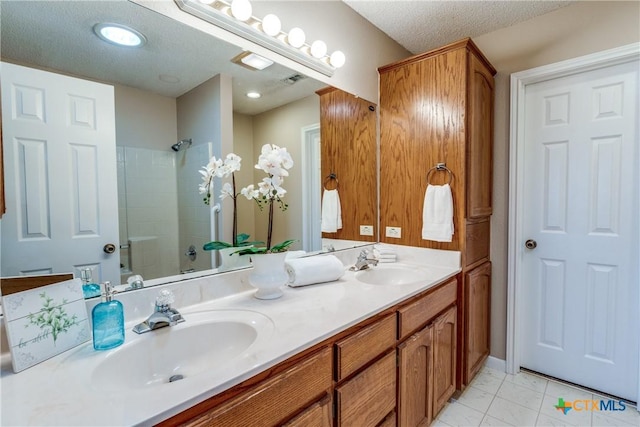 full bath featuring a sink, tiled shower, a textured ceiling, and double vanity