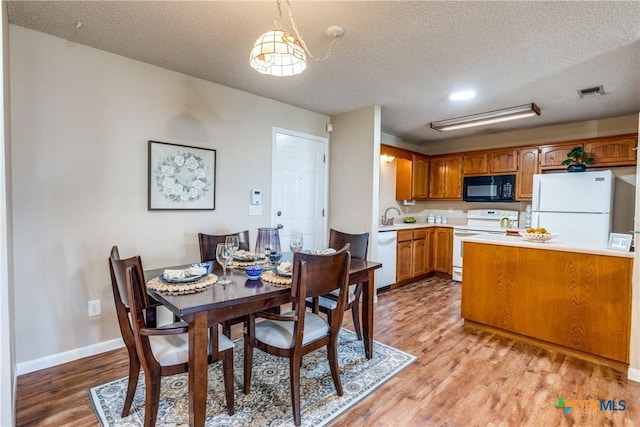 dining space featuring visible vents, a textured ceiling, baseboards, and light wood-style floors