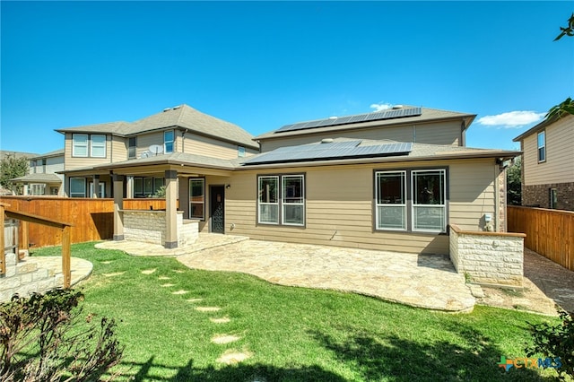 rear view of house with solar panels, a patio area, and a lawn