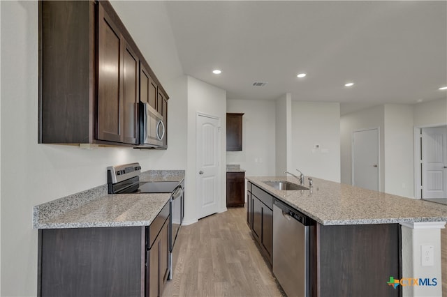 kitchen featuring sink, a kitchen island with sink, stainless steel appliances, light stone countertops, and dark brown cabinets