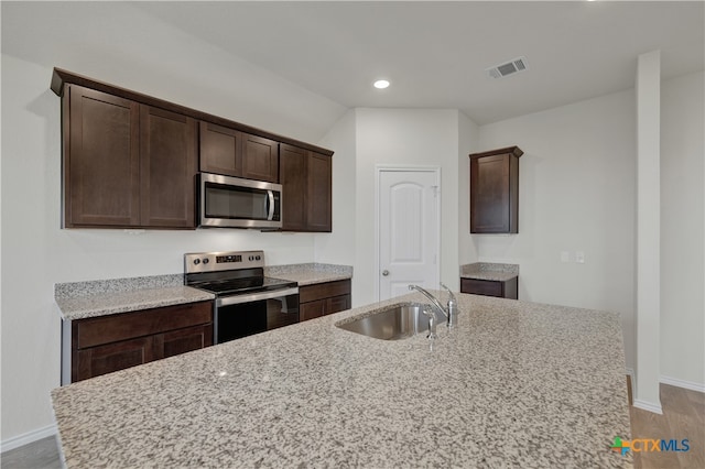 kitchen featuring dark brown cabinetry, sink, light stone countertops, and appliances with stainless steel finishes