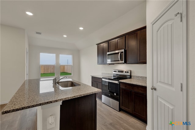 kitchen featuring appliances with stainless steel finishes, sink, a kitchen island with sink, light stone countertops, and dark brown cabinets