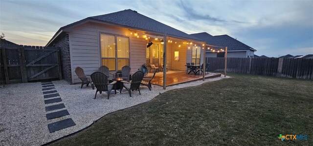 back of house at dusk with an outdoor fire pit, a lawn, a fenced backyard, a patio, and a gate