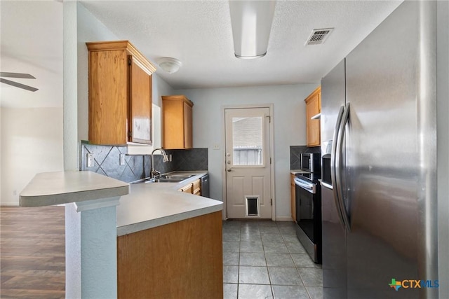 kitchen featuring tasteful backsplash, light countertops, appliances with stainless steel finishes, a peninsula, and a sink