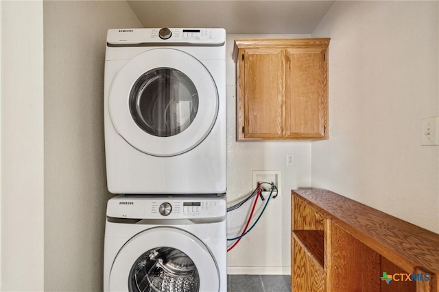 clothes washing area with tile patterned floors, cabinet space, and stacked washer and dryer