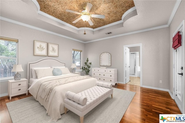 bedroom with ensuite bath, ornamental molding, a raised ceiling, ceiling fan, and hardwood / wood-style floors