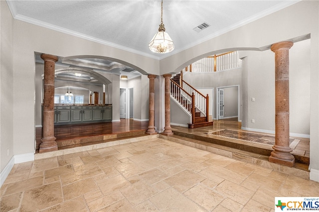 foyer featuring decorative columns, ornamental molding, and a notable chandelier