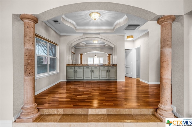 interior space featuring a tray ceiling, ornate columns, hardwood / wood-style floors, and ornamental molding