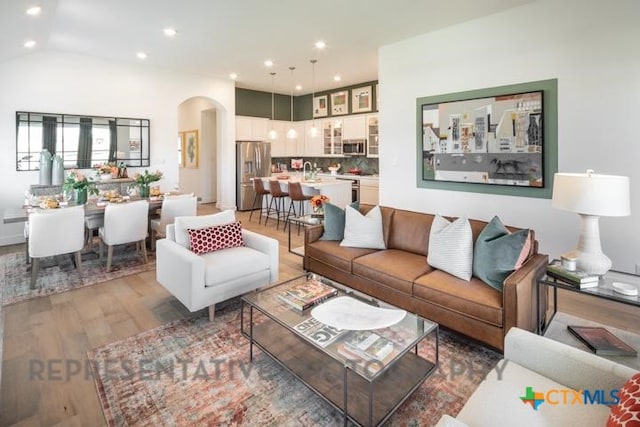 living room with arched walkways, light wood-style flooring, and recessed lighting
