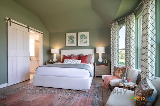 bedroom with lofted ceiling, multiple windows, a barn door, connected bathroom, and wood finished floors