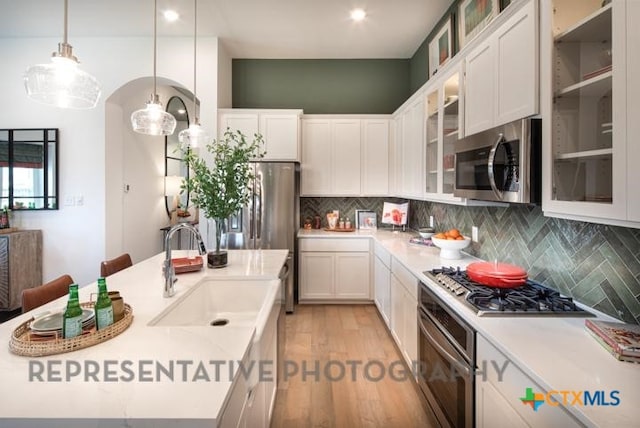 kitchen featuring stainless steel appliances, a sink, light countertops, backsplash, and white cabinetry