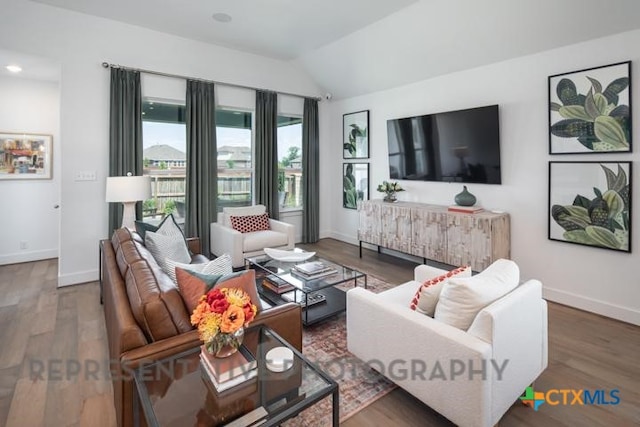 living room featuring vaulted ceiling, baseboards, and wood finished floors